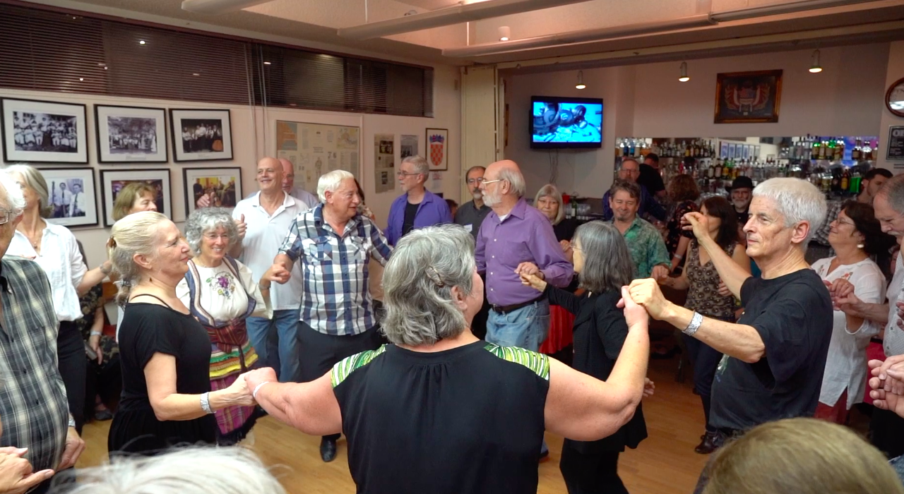 Dancers in a circle with joined hands, festival bar visible in the background