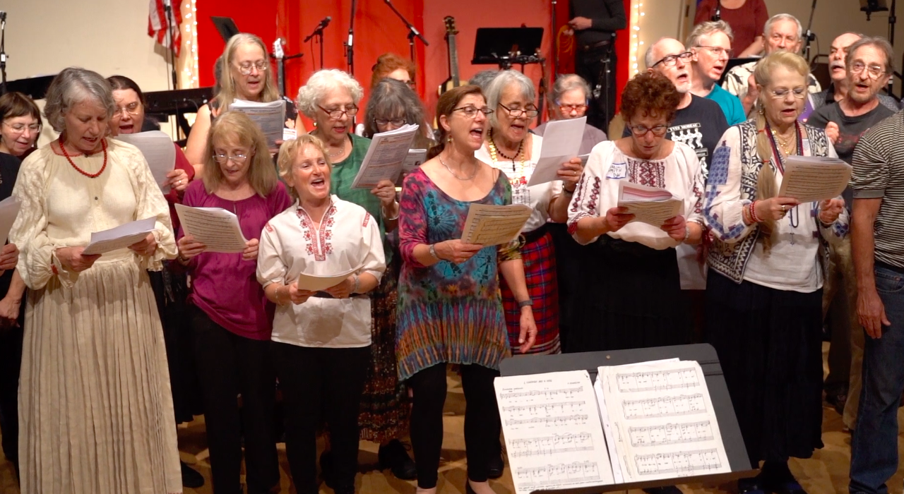 A chorus of women in festive dress singing together